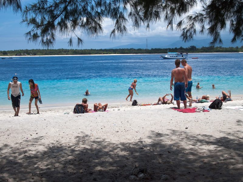 Travellers relaxing on the white-sand beach of Gili Trawangan with turquoise water behind